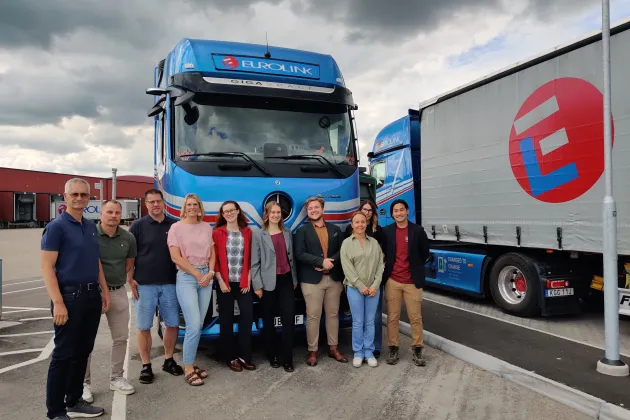 A group of persons standing in front of trucks