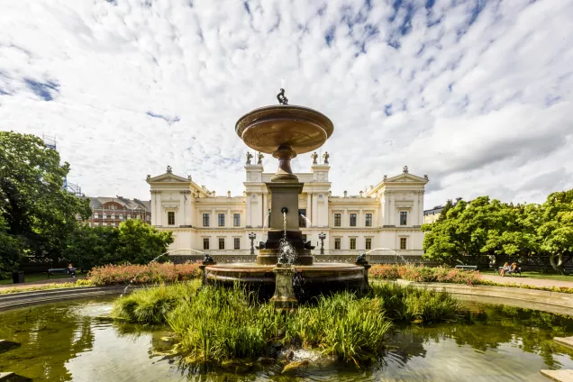 The university building with the fountain in front and clody sky behind. Photo. 