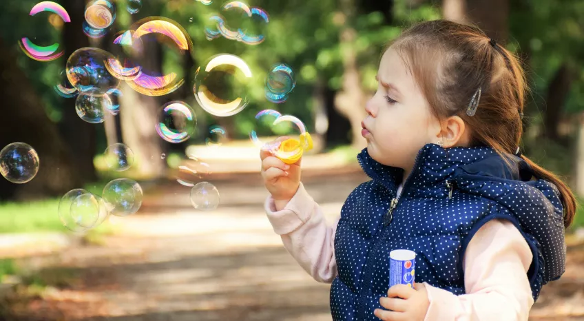 A close up of a young girl - toddler age - blowing soap bubbles.