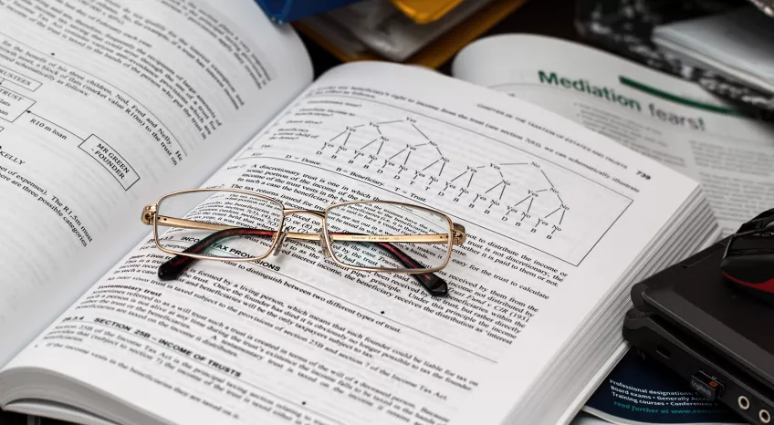 A close up photo of an open textbook with a pair of glasses resting across the pages.