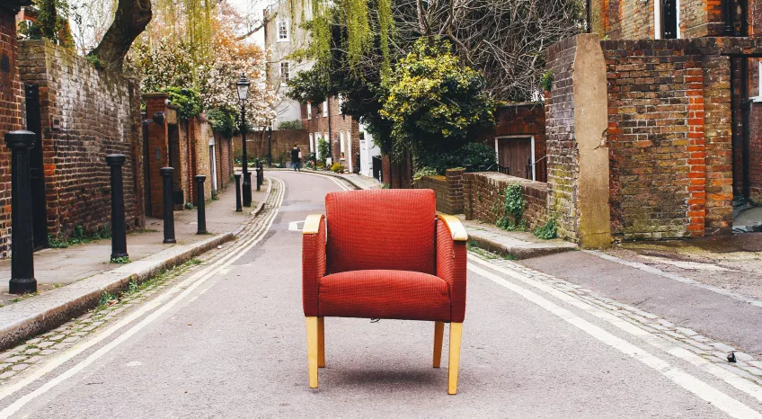 An old red armchair stands abandoned in the middle of a street.