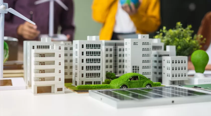 A model car dressed in green leaves drives through a model city in all white.